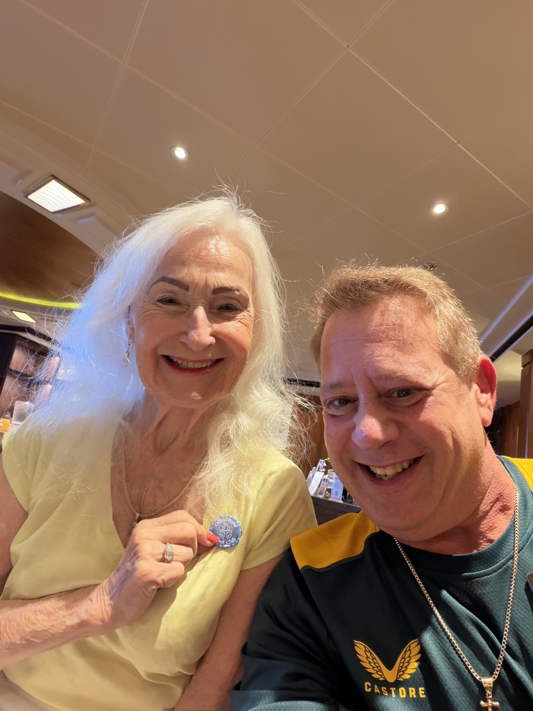 A familiar face on the voyage: Scott A. Astin smiling beside a fellow traveler holding a blue keepsake pin