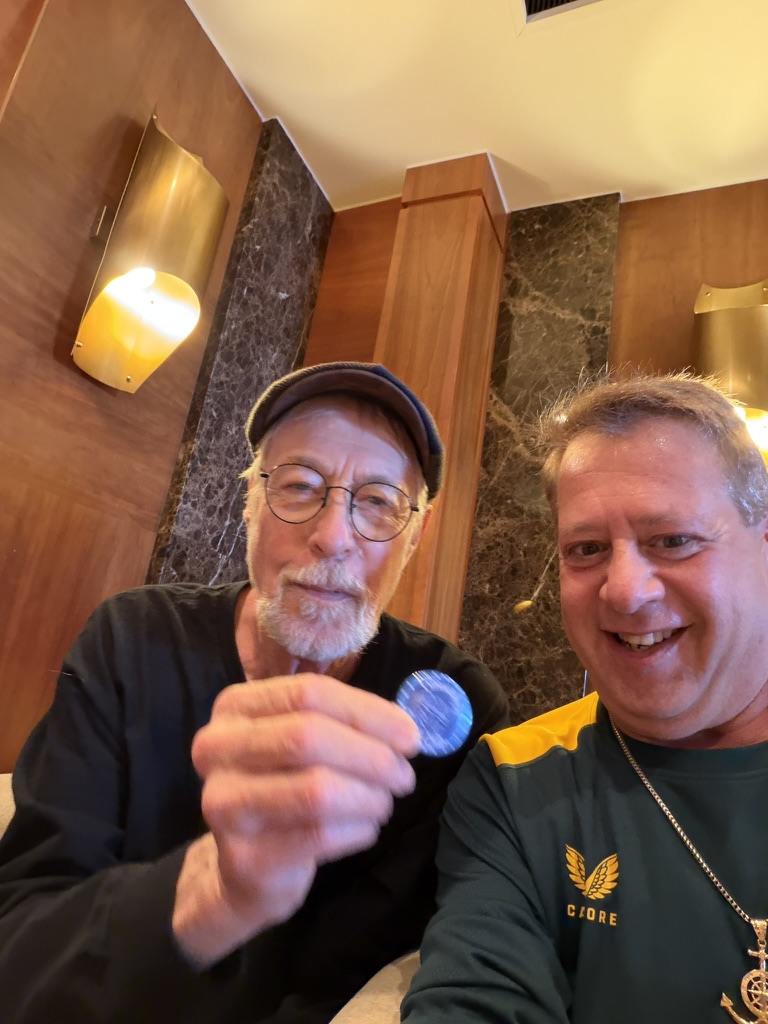 A keepsake shared: Scott A. Astin seated beside a fellow traveler holding a blue keepsake pin