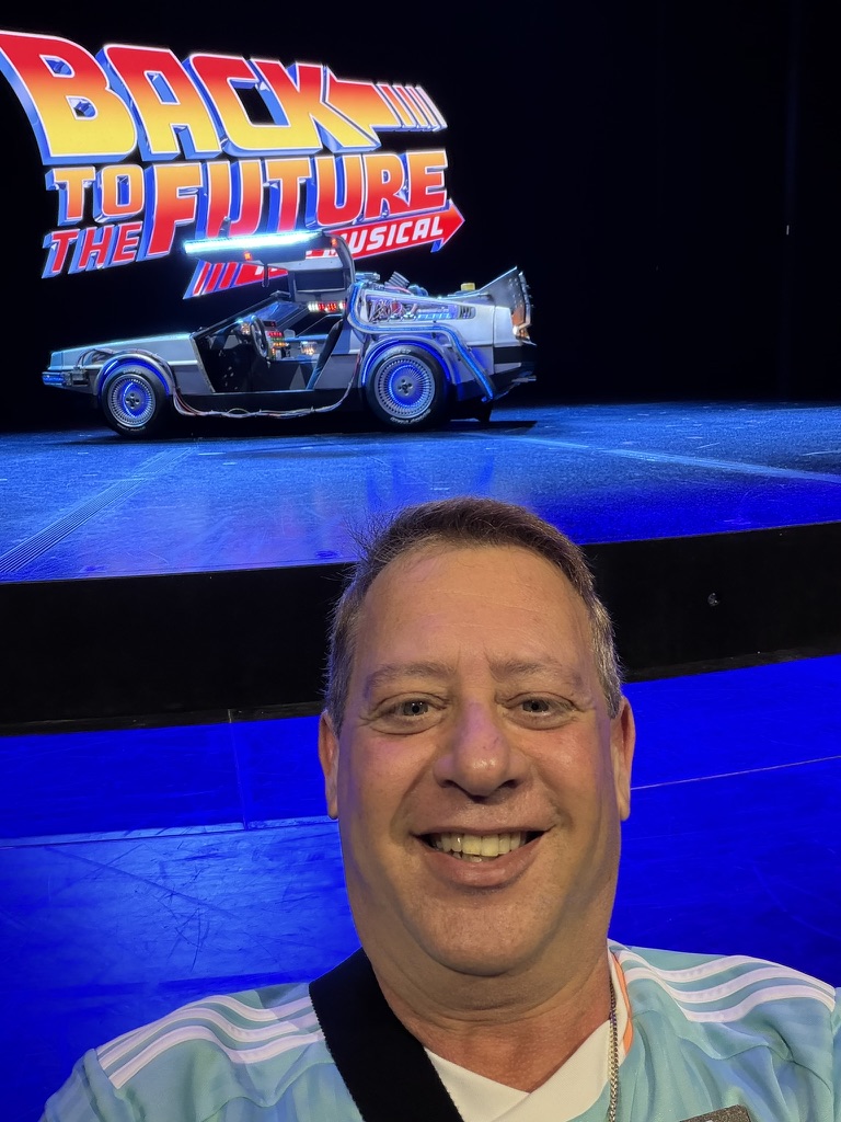 A show worth remembering: Scott A. Astin smiling in front of a Back to the Future stage display