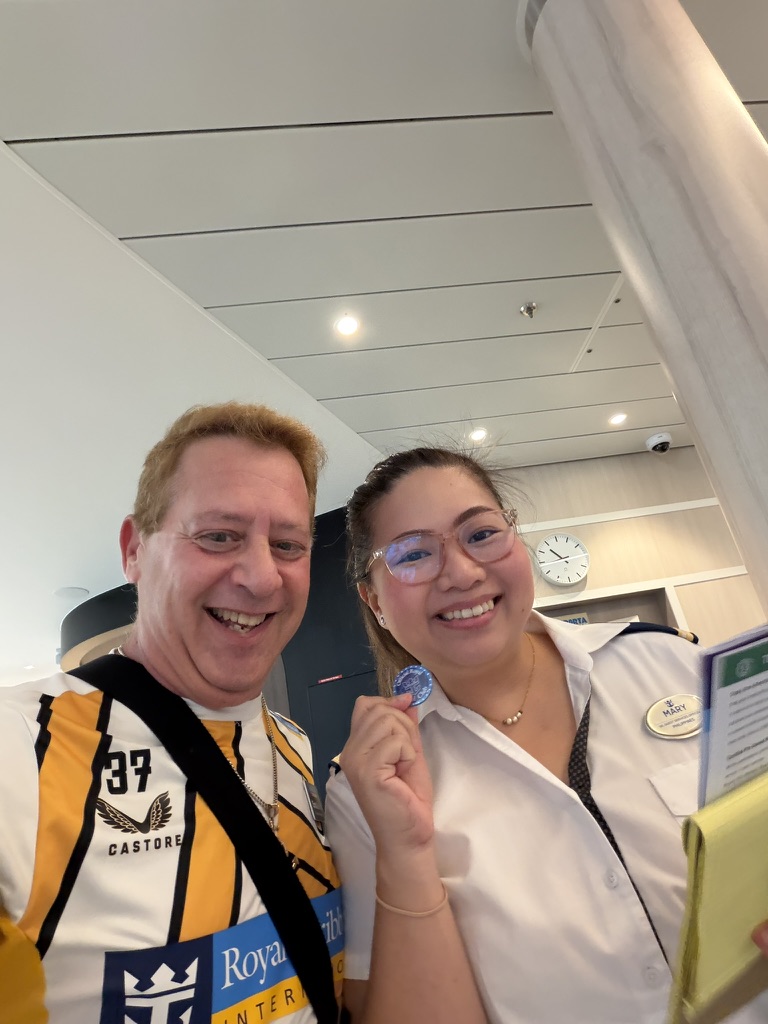 A crew welcome between moments: Scott A. Astin smiling with a uniformed crew member in a bright shipboard interior