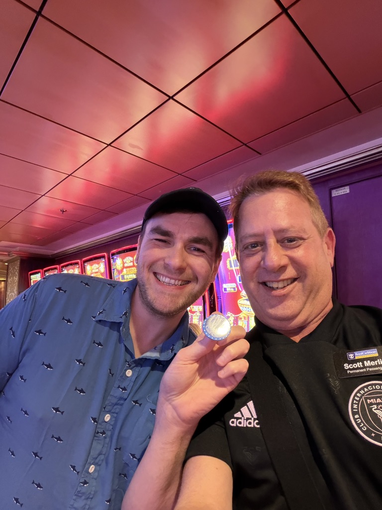 A celebration under the lights: Scott A. Astin beside a fellow traveler holding a blue keepsake pin under red casino lights