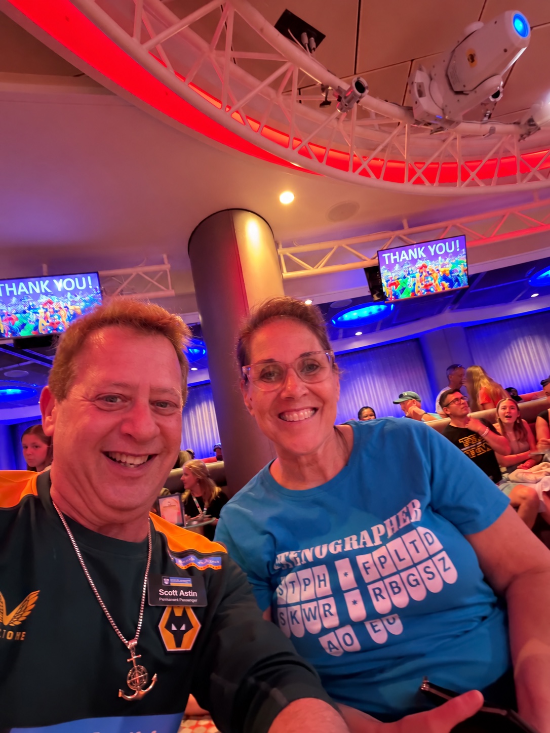A room full of gratitude: Scott A. Astin smiling with a fellow traveler in a theater beneath Thank You screens