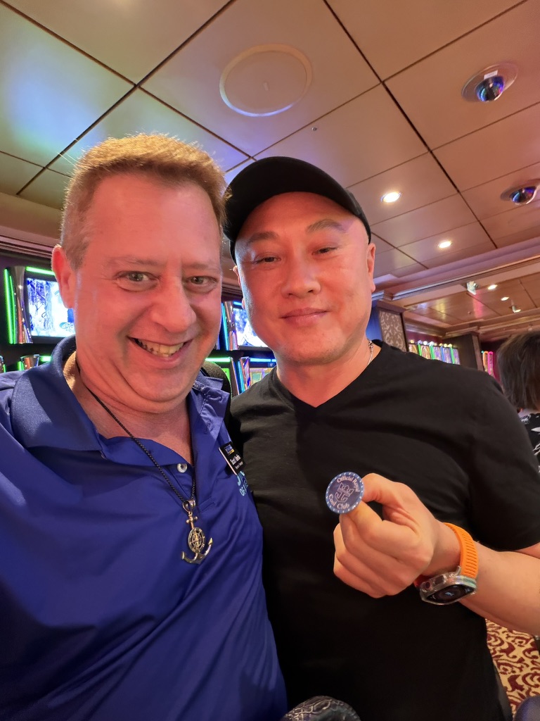 A familiar face and another voyage: Scott A. Astin beside a fellow traveler displaying a blue keepsake pin in the casino