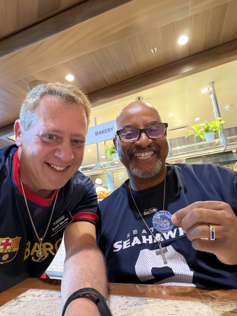 Friends around the table: Scott A. Astin seated beside a fellow traveler in a Seahawks shirt holding a blue keepsake pin