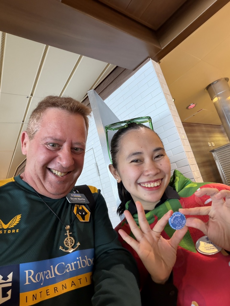 Recognition shared with the team: Scott A. Astin beside a fellow traveler holding a blue keepsake pin near the ship’s windows