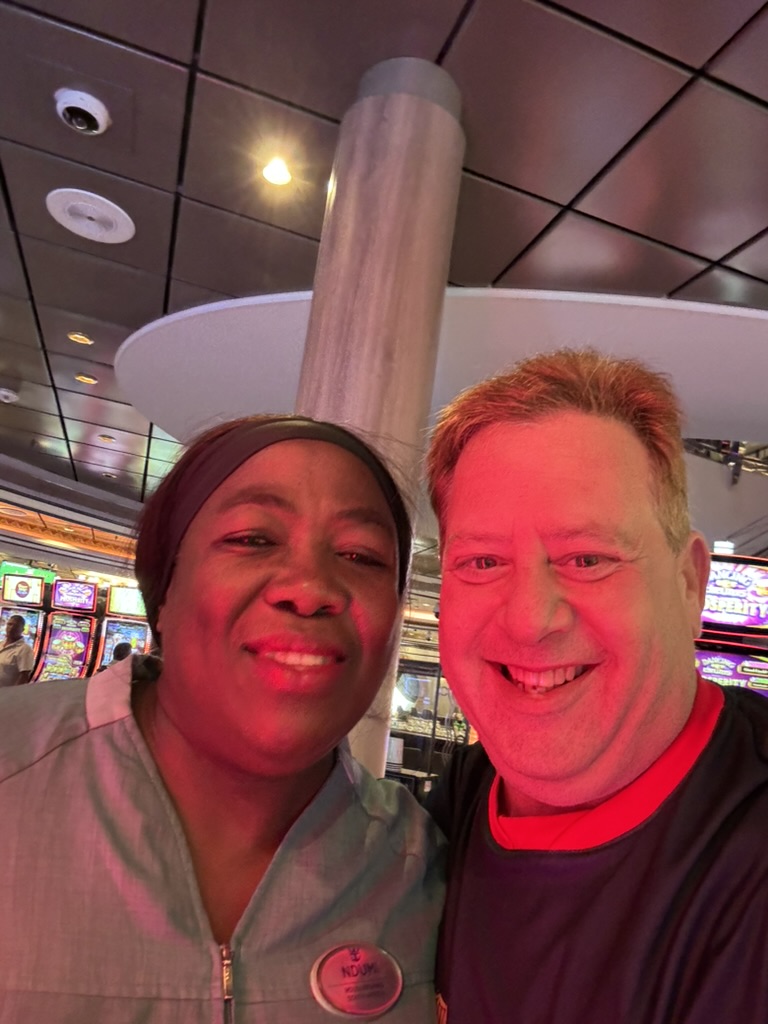 A celebration under red lights: Scott A. Astin smiling with a uniformed crew member beneath red casino lighting