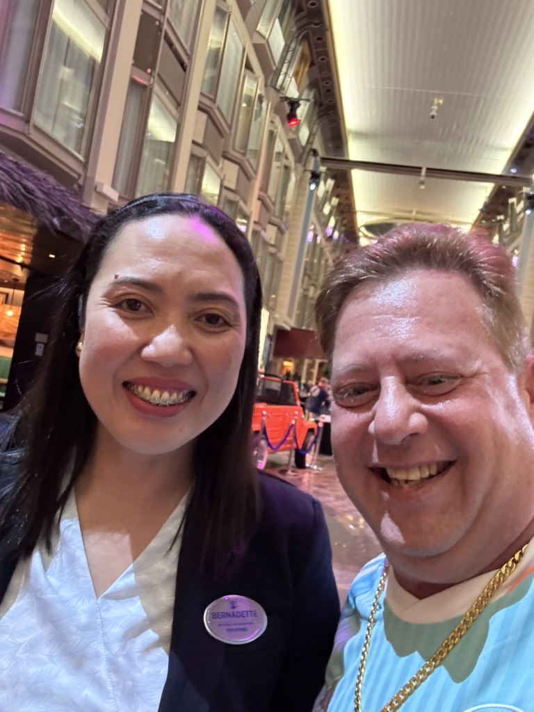 A quiet pause between busy moments: Scott A. Astin smiling with a uniformed crew member in a busy ship atrium