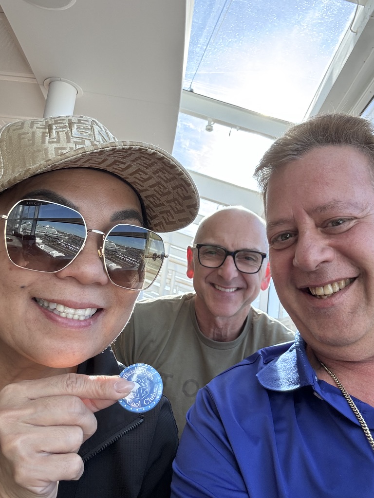 A shared keepsake in the lounge: Scott A. Astin smiling with two fellow travelers, one holding a blue keepsake pin