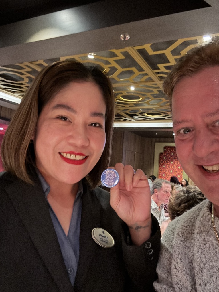 A polished welcome at dinner: Scott A. Astin beside a uniformed crew member holding a blue keepsake pin