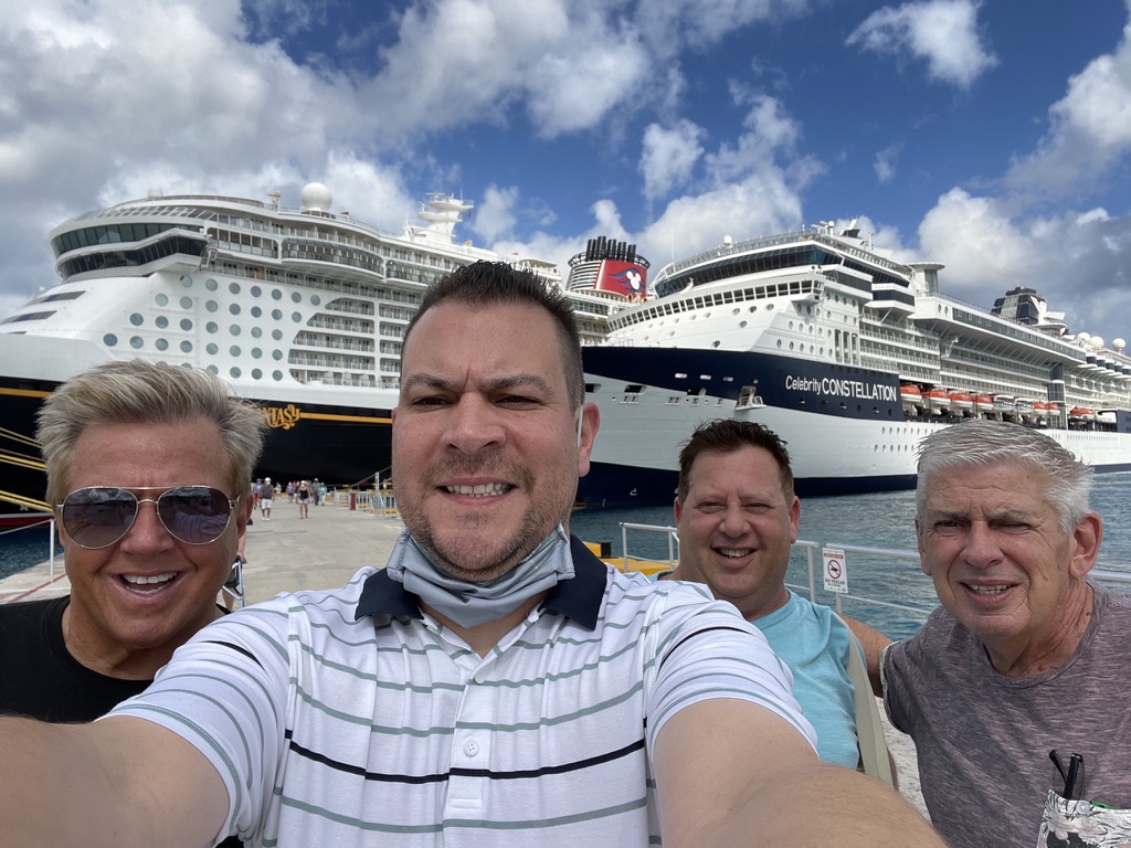 The ship in the background, the people in front: Four travelers taking a port selfie with two cruise ships behind them