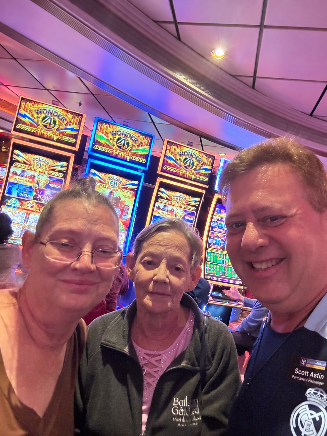 A final frame full of shipboard color: Scott A. Astin smiling with two fellow travelers in front of colorful casino machines