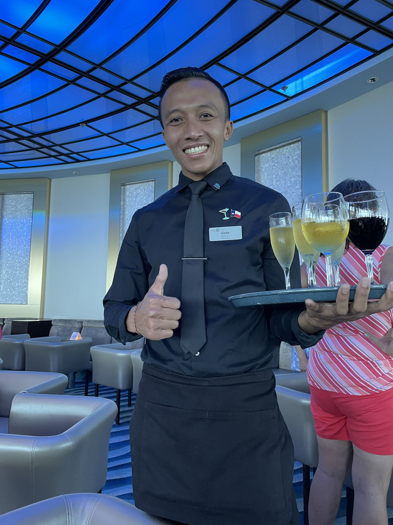 Gede smiling with a tray of drinks in a ship lounge